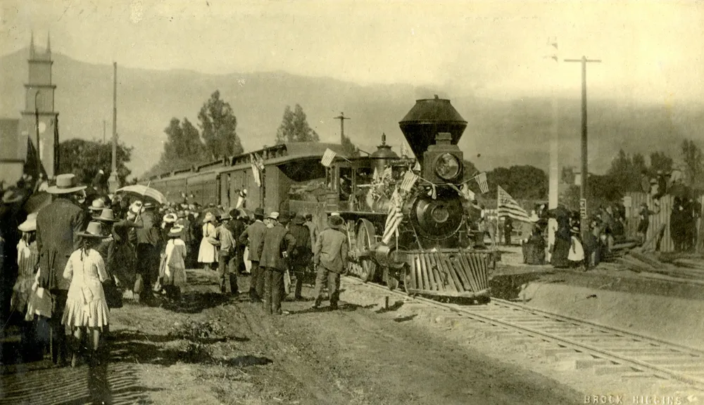 A crowd of people stand to the left of the first train to reach Santa Barbara